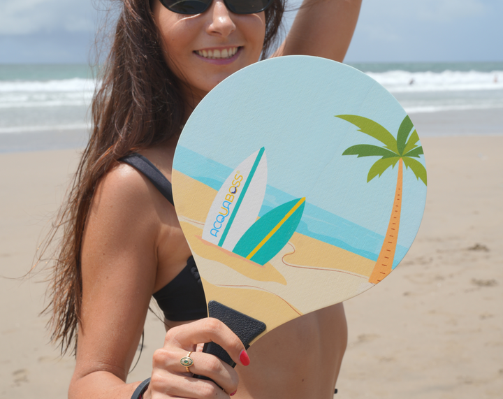 Woman on a beach holding a round fan with a tropical surf design