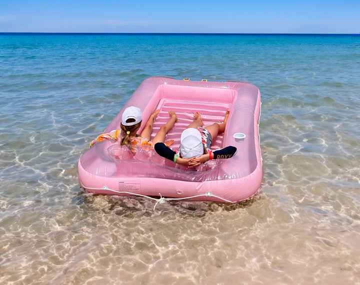 young girls floating in the pink tanning bed float in the beach 