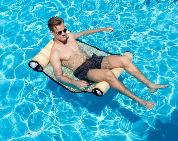 Man relaxing on a pool water hammock float in clear blue water