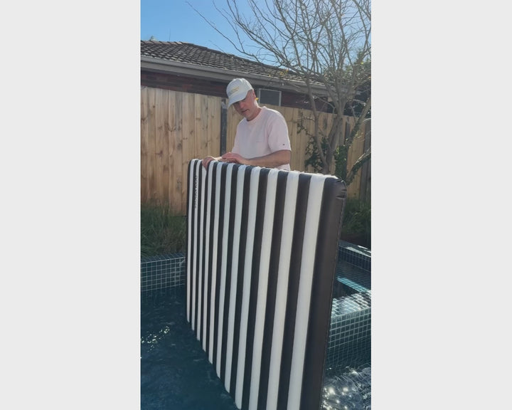 ACQUABOSS black and white inflatable float mat demonstrated poolside, featuring an oversized floating surface, portable design and easy inflation for pool, lake and beach days.