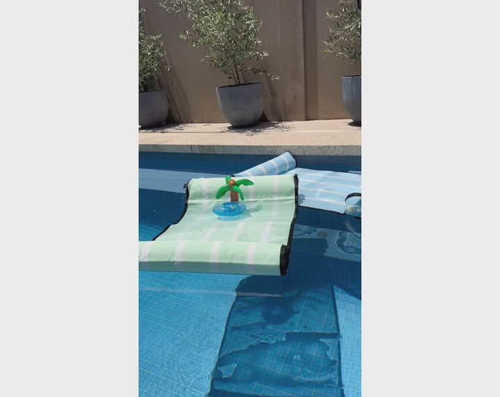 video of  ACQUABOSS floating water hammocks in pastel green and blue resting at the pool’s edge, with an inflatable palm tree drink holder floating between them 