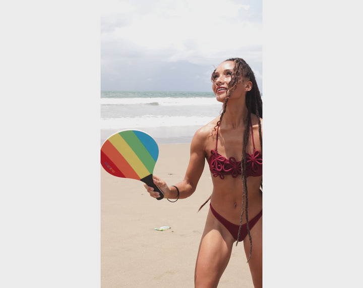Couple playing a rally on the sand with the ACQUABOSS Beach Sunset Paddle Set, using the rainbow-coloured paddles and ball by the shoreline