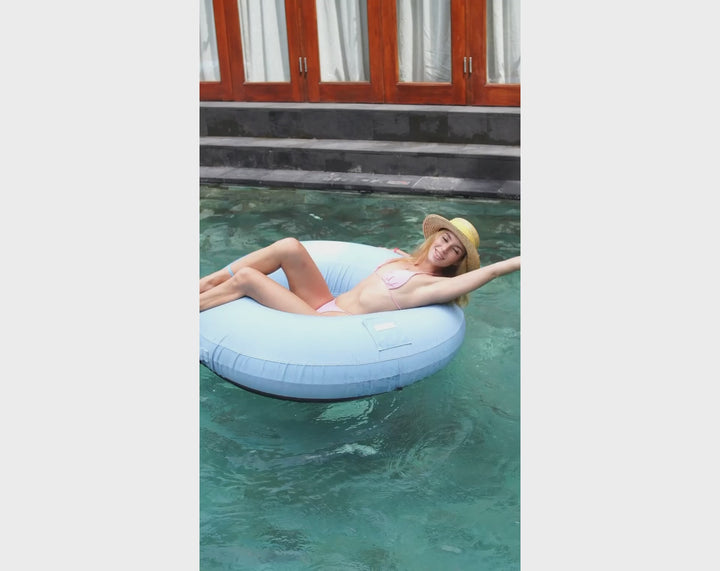 Woman wearing a sun hat lounging on the ACQUABOSS Luxe Inflatable Ring with removable fabric cover, floating elegantly in the pool as part of the Luxe collection